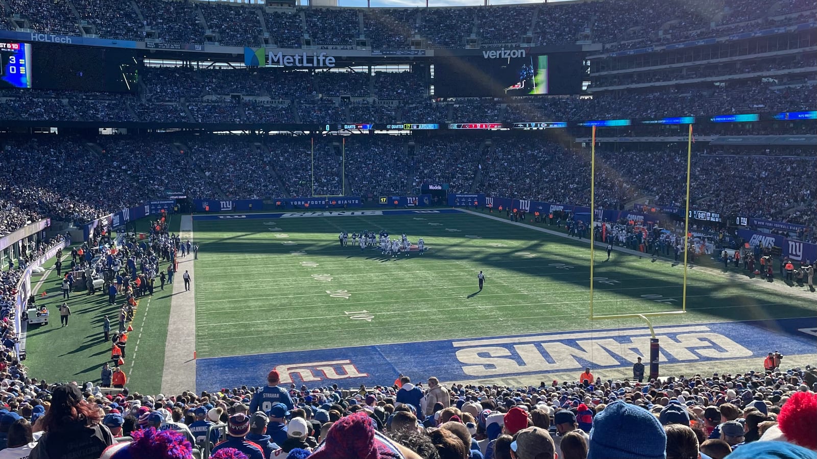 A packed MetLife Stadium seen from the upper stands, with the Giants name painted in the near end zone and players on the field.