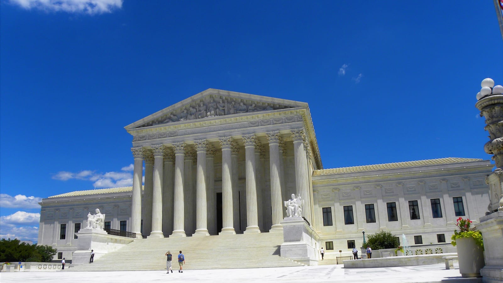 The white marble west front of the Supreme Court Building in Washington, with its columns and broad front steps under a blue sky.